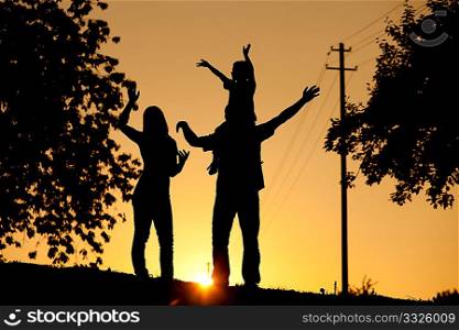 Family having a walk at sunset, the child sitting on his father&acute;s shoulders waving at the viewer; the whole scene is shot back lit, very tranquil and peaceful