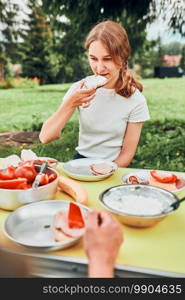 Family having breakfast outdoors on c&ing during summer vacation. Bread, cottage cheese, cold meat, tomatoes, fruits and coffee cups on table. Close up of outdoor table setting set on grass in the garden. Family having breakfast outdoors on c&ing during summer vacation