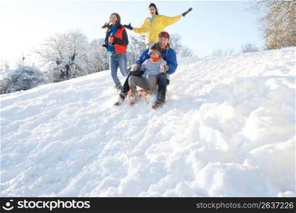 Family Having Fun Sledging Down Snowy Hill
