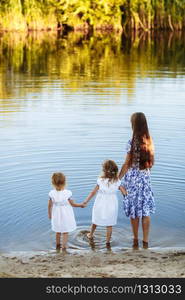 Family having fun together by the lake. Mother with her two daughters is on the walk next to the lake. Family having fun together by the lake. Mother with her two daughters is on the walk next to the lake.