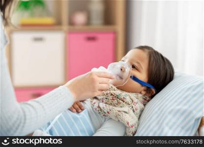 family, health and medicine concept - mother and sick little daughter lying in bed with oxygen mask or nebulizer at home. mother and sick daughter with oxygen mask in bed