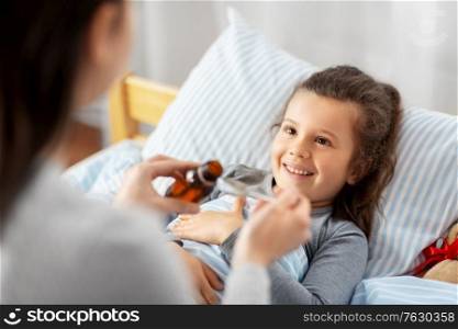 family, health and medicine concept - mother pouring cough syrup for little sick daughter lying in bed at home. mother pouring cough syrup for sick daughter