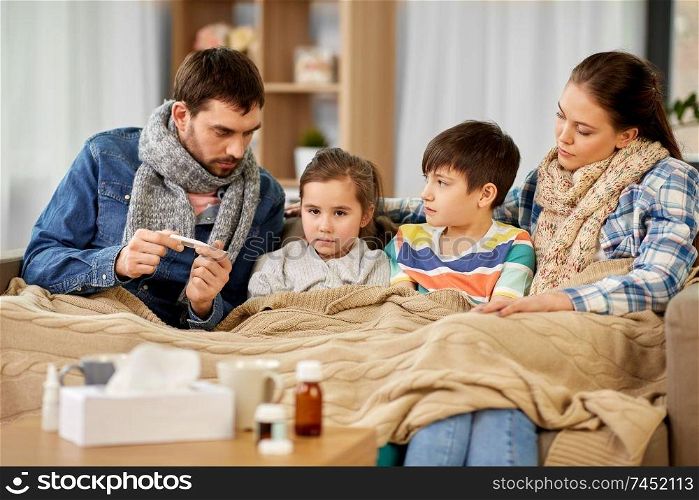family, health and people concept - father with thermometer, mother and ill children having fever at home. family with ill children having fever at home