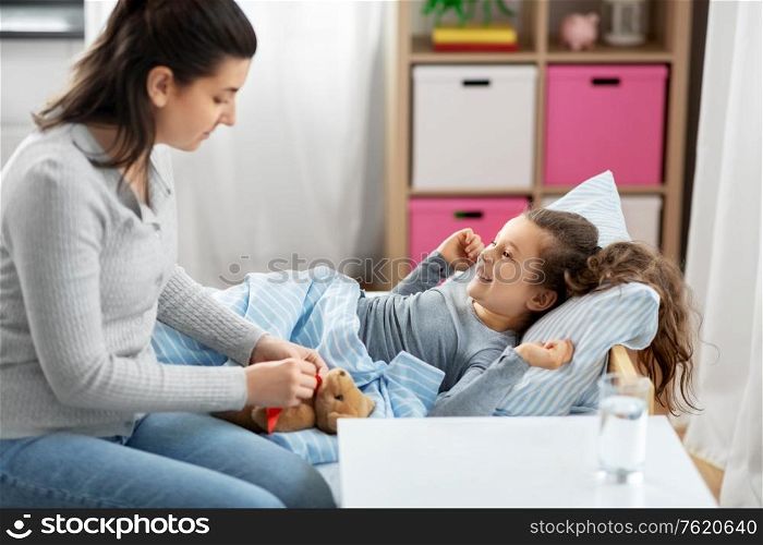 family, health and people concept - mother and happy smiling little daughter lying in bed at home. mother and happy little daughter in bed at home