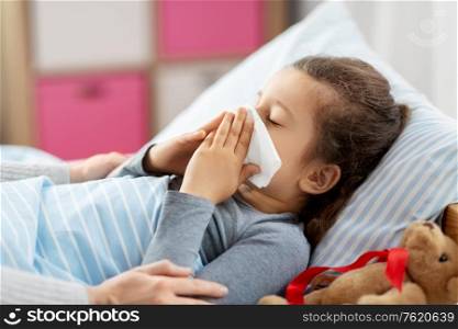 family, health and people concept - mother and sick little daughter lying in bed and blowing nose at home. mother and ill little daughter blowing nose in bed
