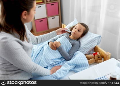 family, health and people concept - mother and sick little daughter lying in bed with oral thermometer and measuring temperature at home. mother and sick daughter measuring temperature