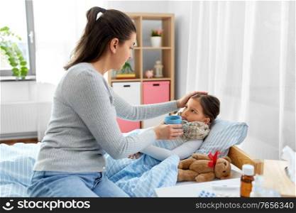 family, health and people concept - mother giving hot tea sick daughter lying in bed at home. mother giving tea to sick daughter lying in bed