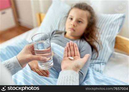 family, health and people concept - mother giving medicine to little sick daughter lying in bed at home. mother giving medicine to sick little daughter