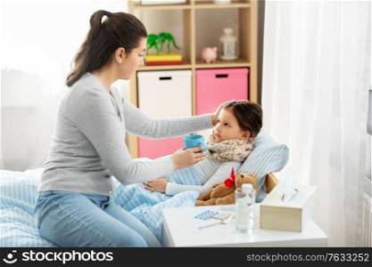 family, health and people concept - mother giving mug with hot tea to sick little daughter lying in bed at home. mother giving hot tea to sick little daughter