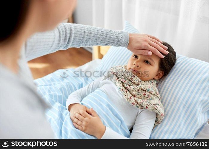 family, health and people concept - mother measuring temperature of sick daughter lying in bed at home with hand. mother measuring temperature of sick daughter
