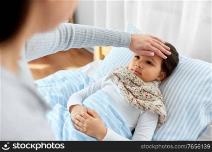 family, health and people concept - mother measuring temperature of sick daughter lying in bed at home with hand. mother measuring temperature of sick daughter