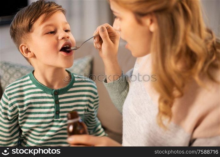 family, health and people concept - sad mother giving antipyretic medication or cough syrup to ill little son at home. mother giving medication or cough syrup to ill son