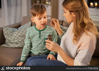 family, health and people concept - sad mother giving antipyretic medication or cough syrup to ill little son at home. mother giving medication or cough syrup to ill son