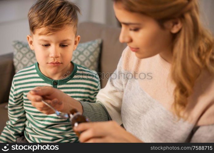 family, health and people concept - sad mother pouring antipyretic medication or cough syrup to spoon for ill little son at home. mother giving medication or cough syrup to ill son