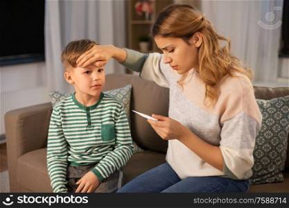family, health and people concept - sad mother with thermometer measuring ill son&rsquo;s temperature at home. sad mother with thermometer and ill son at home