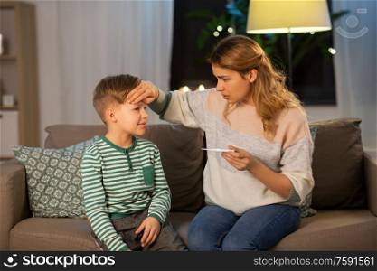 family, health and people concept - sad mother with thermometer measuring ill son&rsquo;s temperature at home. sad mother with thermometer and ill son at home