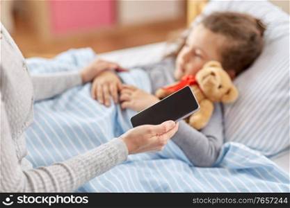 family, health and people concept - sick little daughter sleeping in bed and mother with smartphone measuring temperature with her hand at home. sick daughter and mother with phone at home