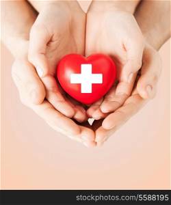 family health, charity and medicine concept - male and female hands holding red heart with cross sign