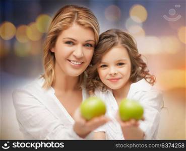 family, healthy eating and food concept - happy mother and daughter with green apples over lights background. happy mother and daughter with green apples