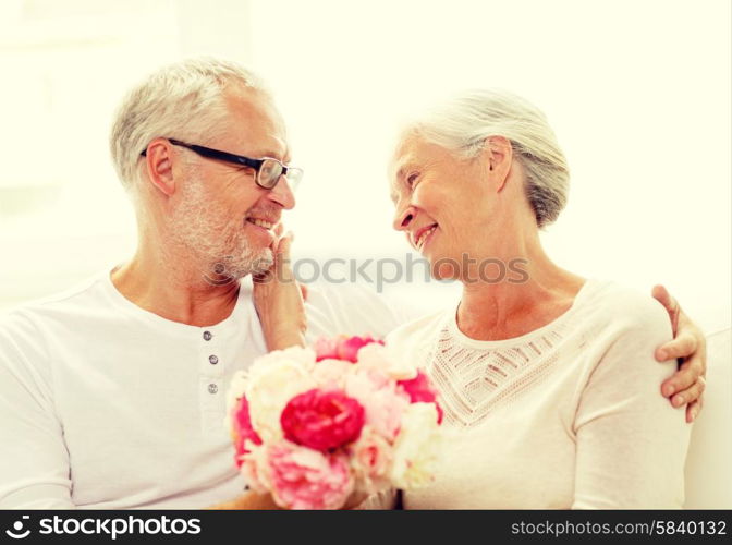 family, holidays, age and people concept - happy senior couple with bunch of flowers at home