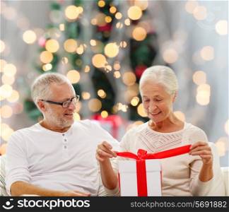 family, holidays, age and people concept - happy senior couple with gift box over christmas tree lights background