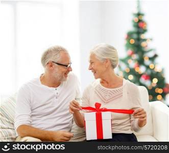family, holidays, age and people concept - happy senior couple with gift box over living room and christmas tree background