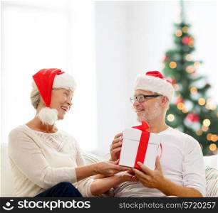 family, holidays, age and people concept - happy senior couple with gift box over living room and christmas tree background
