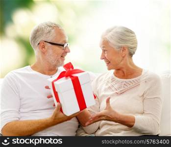 family, holidays, age and people concept - happy senior couple with gift box over green background