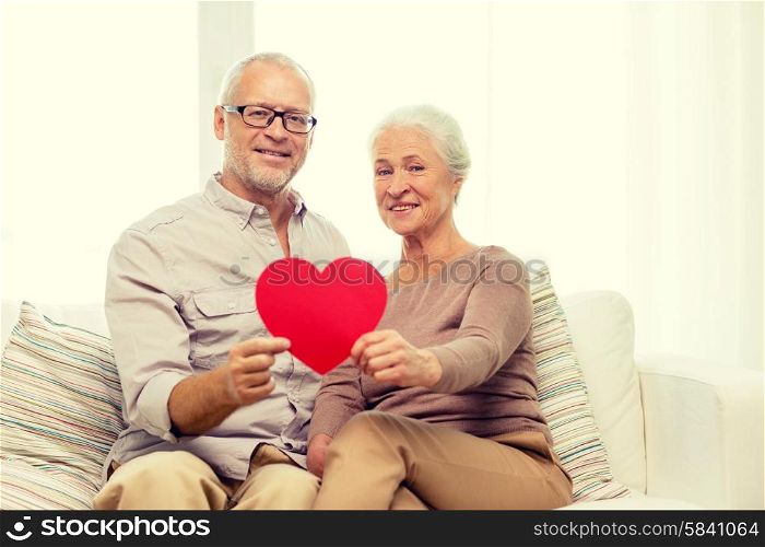 family, holidays, age and people concept - happy senior couple with little red paper heart shape cutout at home