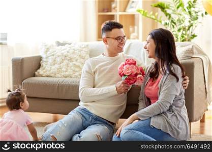 family, holidays and greetings concept - happy husband giving flowers to his wife at home. happy husband giving flowers to his wife at home. happy husband giving flowers to his wife at home