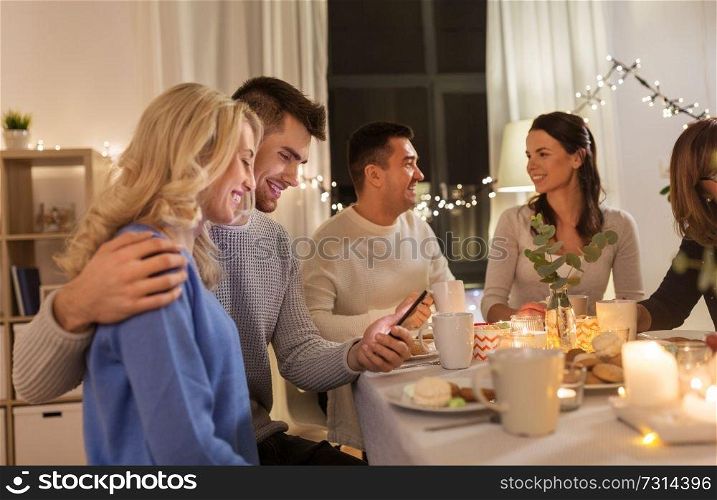 family, holidays and people concept - happy couple with smartphone having tea party at home. happy couple with smartphone at family tea party