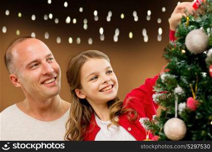 family, holidays and people concept - happy father and daughter decorating christmas tree over lights background. happy family decorating christmas tree at home