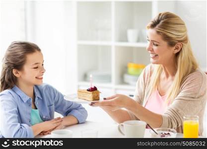 family, holidays and people concept - happy girl and mother holding piece of birthday cake with burning candle at home kitchen. happy family with birthday cake at home kitchen. happy family with birthday cake at home kitchen