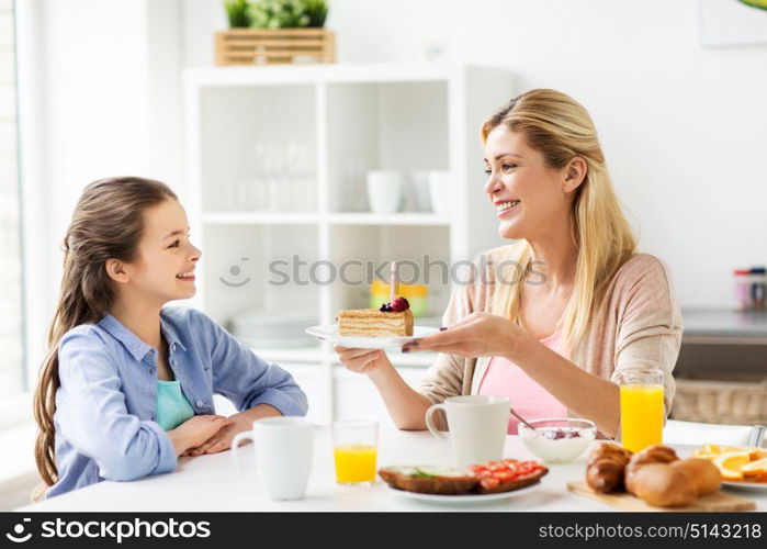 family, holidays and people concept - happy girl and mother holding piece of birthday cake with burning candle at home kitchen. happy family with birthday cake at home kitchen