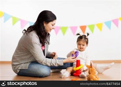 family, holidays and people concept - happy mother and little daughter playing with ring pyramid baby toy on birthday party. mother and baby daughter playing with pyramid toy. mother and baby daughter playing with pyramid toy
