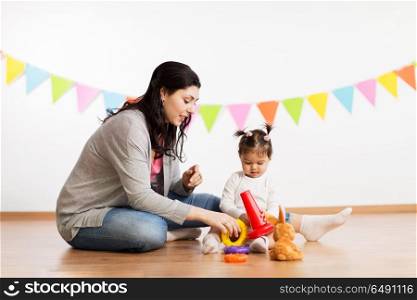 family, holidays and people concept - happy mother and little daughter playing with ring pyramid baby toy on birthday party. mother and baby daughter playing with pyramid toy. mother and baby daughter playing with pyramid toy