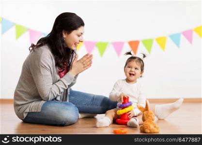 family, holidays and people concept - happy mother applauding for little daughter playing with ring pyramid baby toy on birthday party. mother and baby daughter playing with pyramid toy. mother and baby daughter playing with pyramid toy