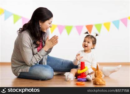family, holidays and people concept - happy mother applauding for little daughter playing with ring pyramid baby toy on birthday party. mother and baby daughter playing with pyramid toy. mother and baby daughter playing with pyramid toy