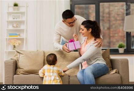 family, holidays and people concept - happy mother, father and baby daughter with birthday present at home. happy family with birthday present at home