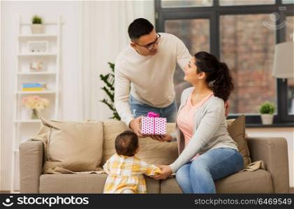 family, holidays and people concept - happy mother, father and baby daughter with birthday present at home. happy family with birthday present at home