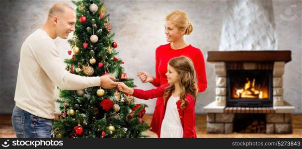 family, holidays and people concept - happy mother, father and daughter decorating christmas tree over home room with fireplace background. mother, father and daughter at christmas tree