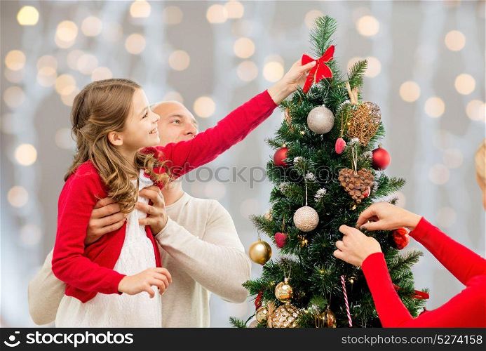 family, holidays and people concept - happy mother, father and daughter decorating christmas tree over lights background. mother, father and daughter at christmas tree