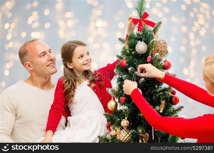 family, holidays and people concept - happy mother, father and daughter decorating christmas tree over lights background. mother, father and daughter at christmas tree