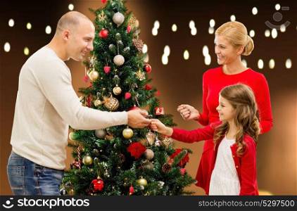 family, holidays and people concept - happy mother, father and daughter decorating christmas tree over lights background. happy family decorating christmas tree at home