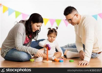 family, holidays and people concept - happy mother, father and little daughter playing with ring pyramid baby toy on birthday party. baby girl with parents playing with pyramid toy. baby girl with parents playing with pyramid toy