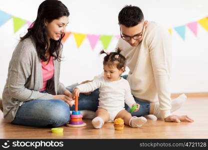 family, holidays and people concept - happy mother, father and little daughter playing with ring pyramid baby toy on birthday party. baby girl with parents playing with pyramid toy. baby girl with parents playing with pyramid toy