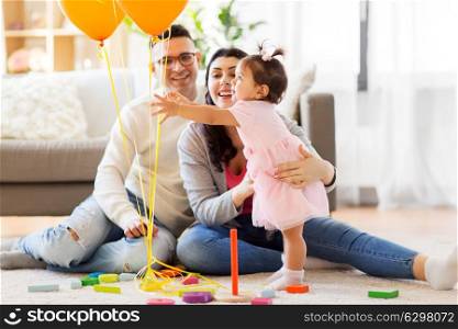 family, holidays and people concept - happy mother, father and little daughter reaching to balloons at home birthday party. baby girl reaching to balloons at birthday party. baby girl reaching to balloons at birthday party