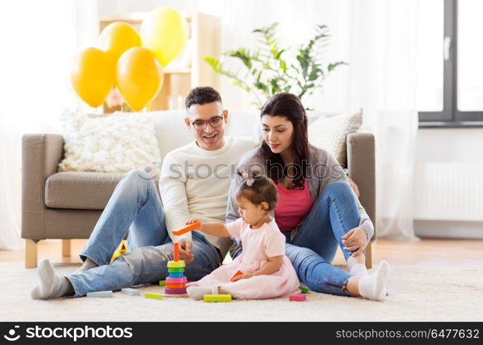 family, holidays and people concept - happy mother, father and little daughter playing with ring pyramid baby toy on birthday party at home. baby girl with parents playing with pyramid toy. baby girl with parents playing with pyramid toy