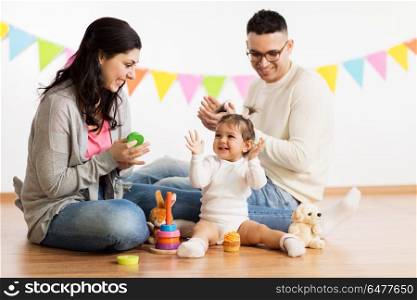 family, holidays and people concept - happy mother, father and little daughter with toys playing and clapping hands on birthday party. baby girl with parents playing and clapping hands. baby girl with parents playing and clapping hands
