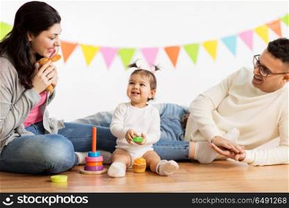 family, holidays and people concept - happy mother, father and little daughter playing with toys on birthday party. baby girl with parents playing with toys. baby girl with parents playing with toys